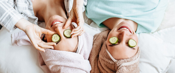 Two girls make homemade face and hair beauty masks. Cucumbers for the freshness of the skin around...