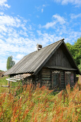 Obraz premium old wooden house in the abandoned village in the green grass under blue summer sky