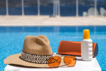 orange coloured beach accessories near swimming pool. Sun cream, sunglasses, music speaker and...
