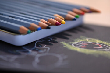 Farbige Buntstifte in einer Schachtel und ein von Kindern gemaltes Bild auf einem Schreibtisch
