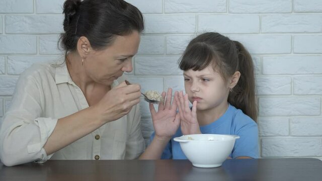 Tasteless cereal. The mother feeds her daughter with porridge, she refuses to eat it.