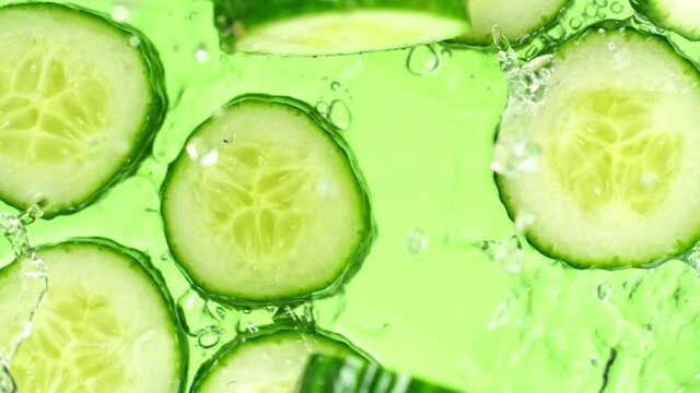 Super Slow Motion Shot of Cucumber Slices Falling into Water on Green Background at 1000fps.