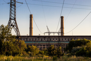 Abandoned thermal power plant with chimneys and power lines against the backdrop of blue sky and nature.