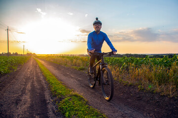 Naklejka premium cyclist on bike rides along the fields of wheat in the sunlight. sports and hobbies. outdoor activities