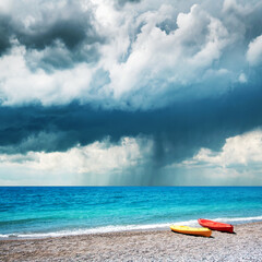 Two kayaks on sea edge. Dramatic storm clouds with rain on background. Summer time