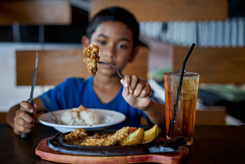 Fototapeta na wymiar Asian boy holding knife and fork cutting grilled Chicken steak on stoned plate in restaurant