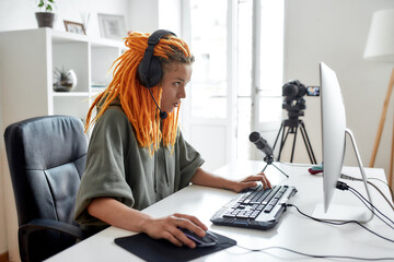 Female esport gamer, woman in headphones looking focused, playing online video game on PC while recording, filming vlog in the daytime © Svitlana