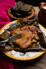 Mexican tamales in banana leaves on wooden background