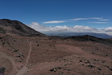 Rocky landscape showing the barren land covered in boulders and brown sand with a mountainous background