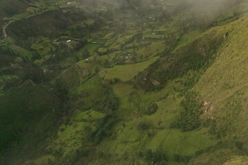 Aerial view of a small green canyon covered in green fields and small patches of forest with a few clouds