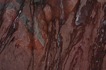 Abstract view of a small gletser with meltwater at a cliff that has different shades of red and grey and a small amount of snow