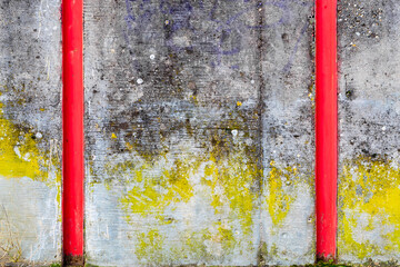 A painted concrete wall as a background. A gray concrete wall with rest of blue, yellow, violet paints, black moss, and two parallel red steel channel beams serving for damming fastening during flood.