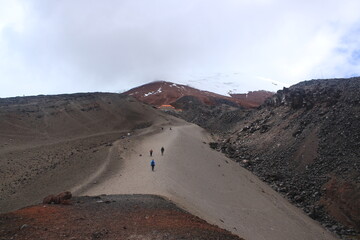 The sandy road to the Cotopaxi �. House with tourists walking on it and the vulcano in the background covered in mist