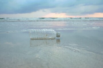 A plastic bottle of drinking water littering on a sea beach with water waves for an environmental cleaning concept 