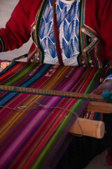 A colorfull andean cloth or rug being woven by a woman in a typically indigenous dress