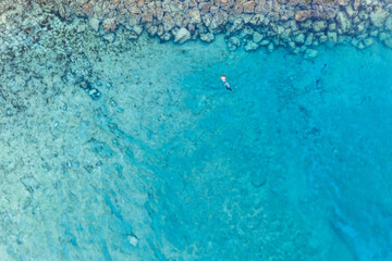 An aerial view of the beautiful Mediterranean Sea and a swimmer, where you can see   the cracked rocky textured underwater corals and the clean turquoise water of Protaras, Cyprus, 