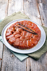 Traditional French tarte tatin with apples and vanilla offered as close-up on a modern Nordic design plate with rustic wooden background