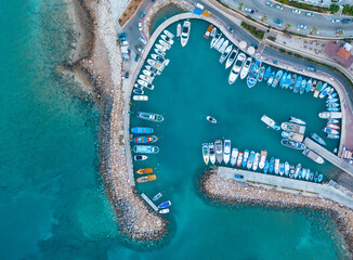 An aerial view of boats docked at a beautiful rocky pier in the Mediterranean sea, where you can se the rocky textured underwater corals and the clean turquoise water of Protaras, Cyprus	