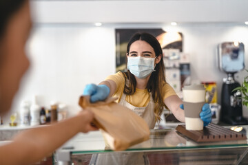 Bar owner working only with take away orders during corona virus outbreak - Young woman worker wearing face surgical mask giving takeout meal to customers - Healthcare and Food drink concept