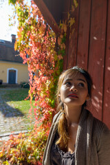 Young beautiful Asian woman thinking against wooden wall in front of elegant suburban house