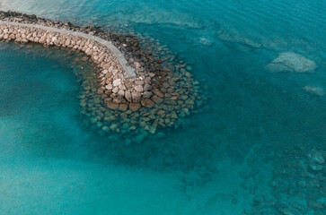 An aerial view of a beautiful walkway surrounded by rocks in the Mediterranean sea, where you can se the rocky textured underwater corals and the clean turquoise water of Protaras, Cyprus	