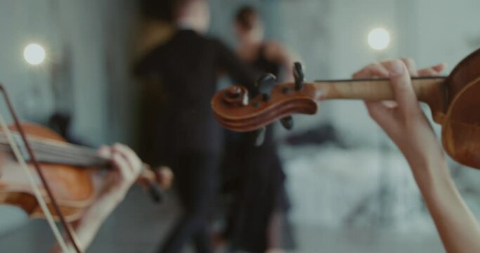 Close view of musicians playing the violins on blurred background of dancers
