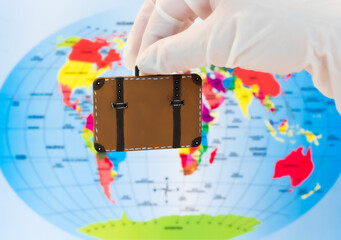 
hand with latex glove holding a suitcase with a world map as background. 
Travel safely in the new normal. Travel and prevention during the pandemic concept