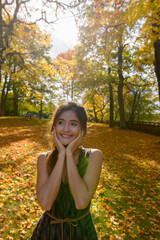 Young happy Asian woman smiling while thinking surrounded by scenic autumn trees in the forest