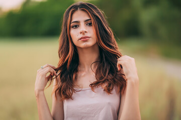 Fototapeta premium Portrait of beautiful sexy young woman with long brown hair in pink tank top and denim shorts posing outdoors, sensual, serious