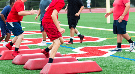Football players running sideways over barriers during high school summer camp