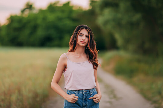 Portrait of beautiful sexy young woman with long brown hair in pink tank top and denim shorts posing outdoors, sensual, serious