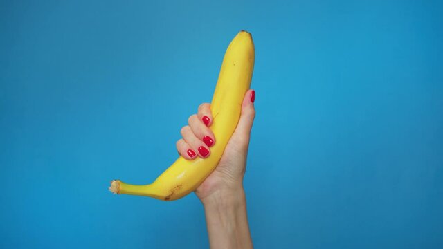 Close up woman's hand crush banana on blue background. Concept video, allegory