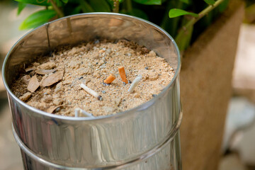Many cigarette stub in sand ashtray. The rest of cigarettes in the ashtray. There are many types of cigarette stub on the sand in the ashtray. A cigarette is not good for health. 