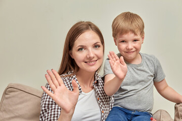 Mom and son are chatting online and waving hello. Look into the camera.