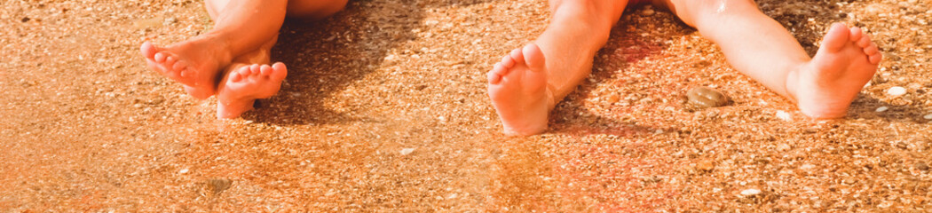Children's feet on the sand by the sea. Horizontal image.