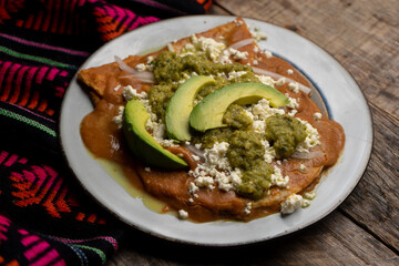 Mexican enfrijoladas with green sauce on wooden background