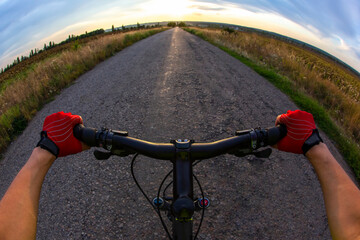 Fototapeta na wymiar Cyclist in red gloves rides on the road towards sunny sunset sky. Sports and travel.