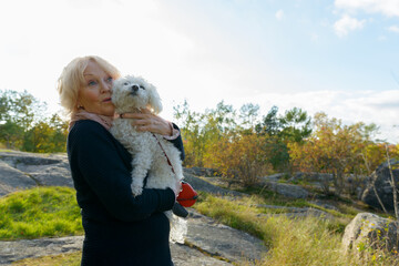 Senior woman looking shocked while holding dog on boulder in the mountains