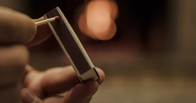 Striking and lighting wooden match in slow motion in front of a fireplace burning. Slow motion 120 fps. 4k graded from RAW. 