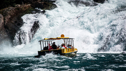 Naklejka premium Schiff mit Personen nähern sich einem Wasserfall auf Welligem Wasser | Rheinfall Schweiz