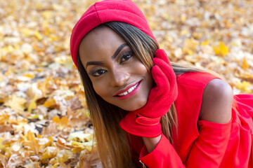 Beautiful African girl in red clothes resting in autumn leaves
