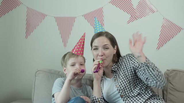 Child blows into toot and looks into camera. Happy family celebrates birthday