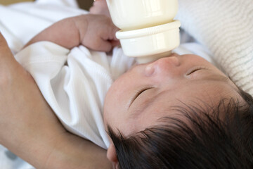 Obraz na płótnie Canvas 母親に抱かれ、哺乳瓶からミルクを飲む生後一ヶ月の赤ちゃん