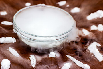 White cool dry ice (frozen carbon dioxide) with smoke effect in the glass bowl on the dark brown wooden background.