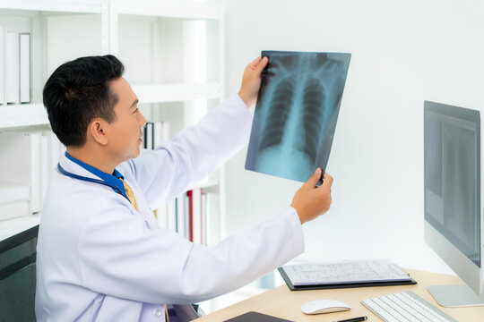 Asian man doctor holding and looking to examining x-ray of the patient’s lungs and brain in a medical clinic at hospital.