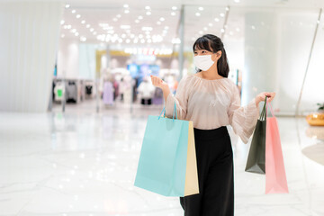 Asian woman wearing mask over her face while walking at shopping mall with shopping bag for...