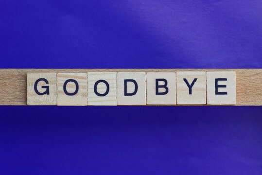 text on gray word goodbay in small wooden letters with black font on a lilac background