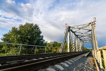 Fototapeta premium Railway bridge over the river at sunset in summer. Wide angle view. Background of blue sky.