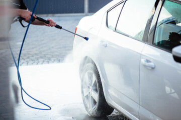 Summer car wash. Cleaning the car using high pressure water. Car wash with soap. Close up concept. Close up photo of a man hands washes his car Concept disinfection and antiseptic cleaning. Car wash.