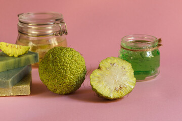 Green Osage apple fruit whole and cut, cream and natural soap from a plant, on a pink background. Close up